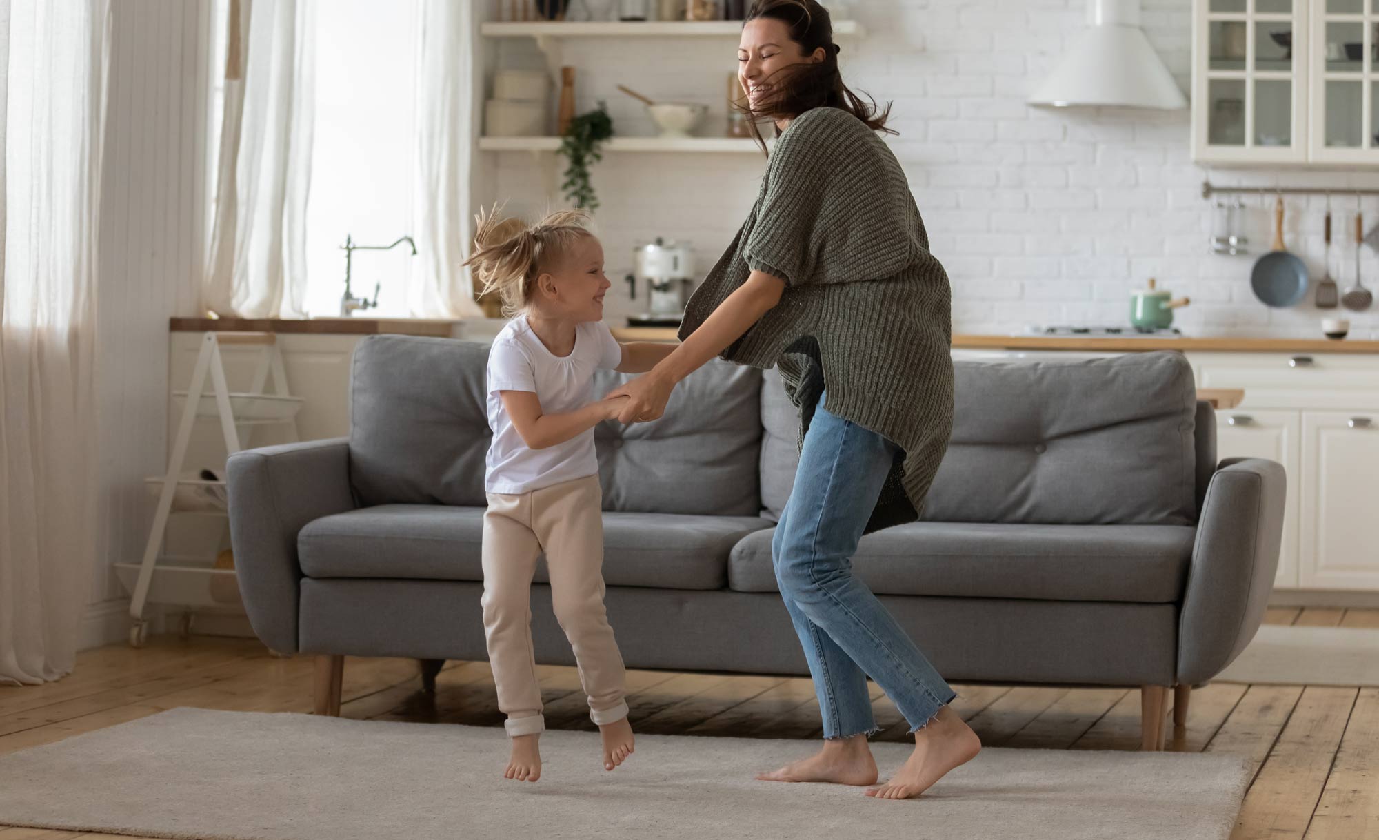 Adult and child jumping together in a bright living room.