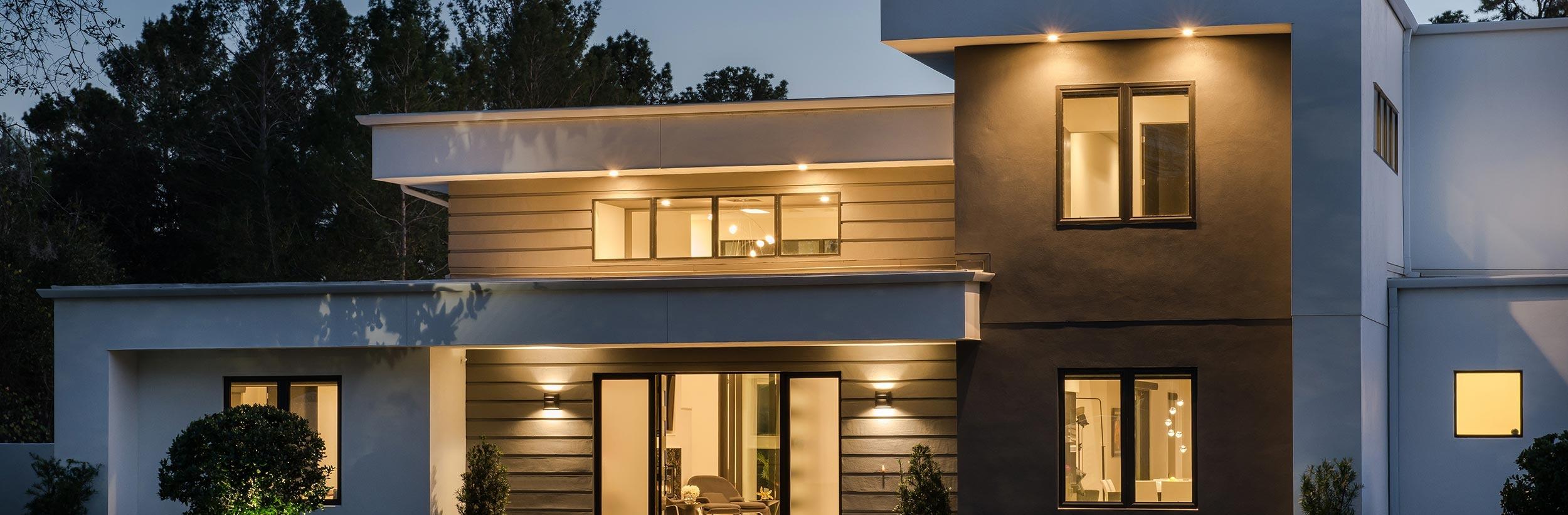 A modern, two-story luxury home beautifully illuminated with warm exterior architectural lighting at dusk.