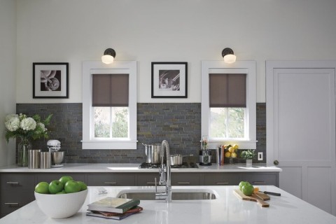 A kitchen with lighting fixtures above two windows and motorized shades.