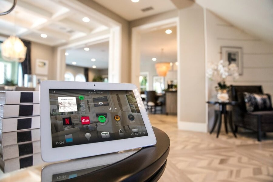 A Control4 interface on a touchscreen tablet sitting on a table at the forefront with a grand living space behind it.