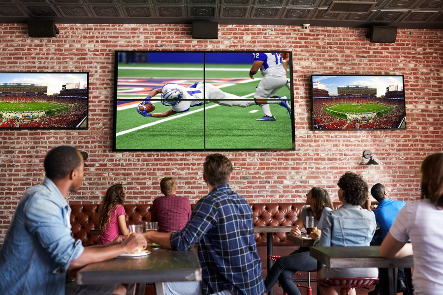 restaurant patrons looking at three wall-mounted flat screen TVs showing a football game playing