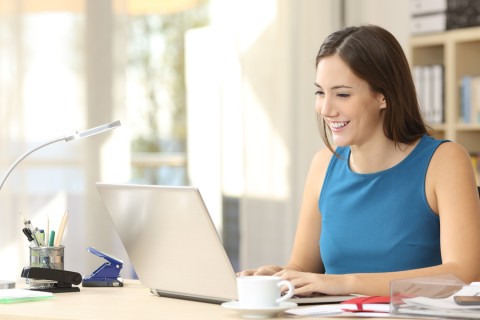 A woman working at a laptop computer in a home office. 