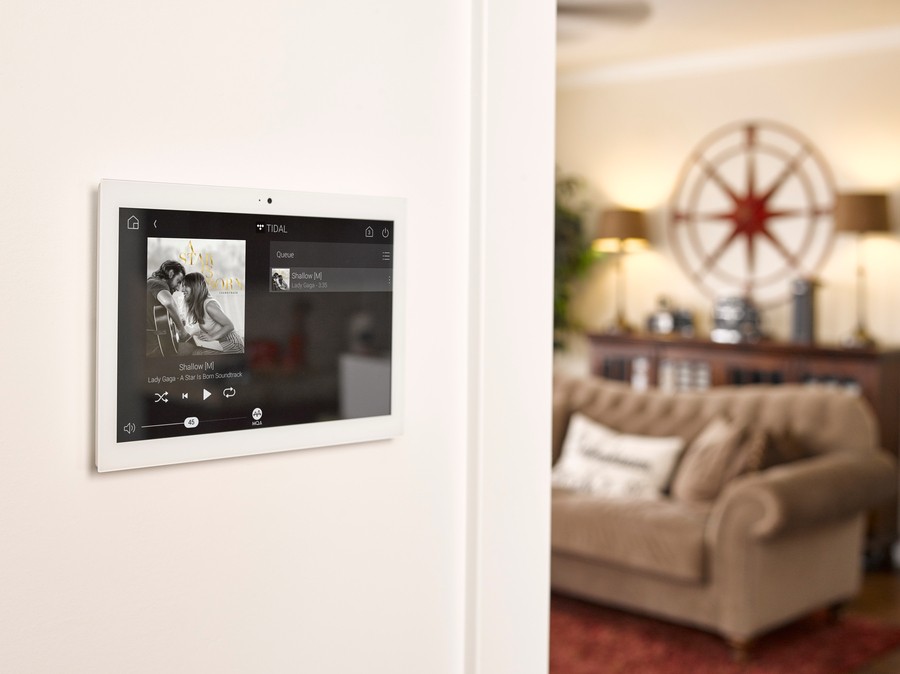 A Control4 wall panel showcasing a whole-home audio interface with music playing.