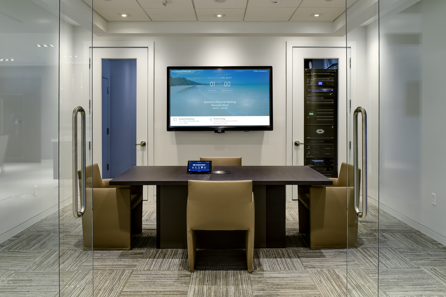 A boardroom with a table and chairs, also featuring conference room AV including a large screen display.