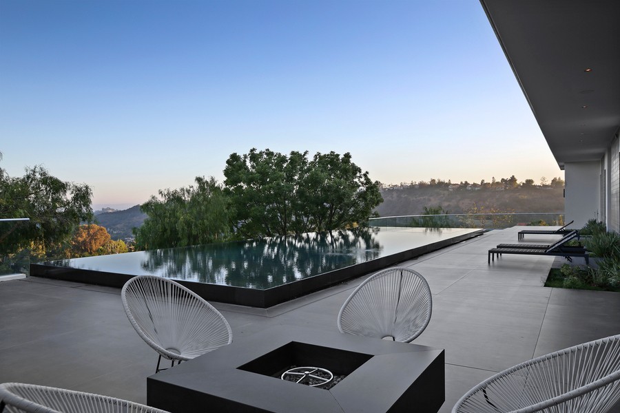 outdoor seating space with an infinity pool in the background, overlooking hills.