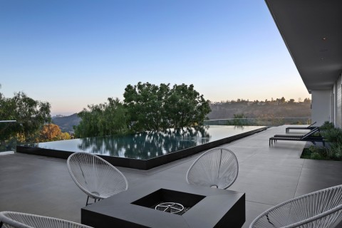 outdoor seating space with an infinity pool in the background, overlooking hills.