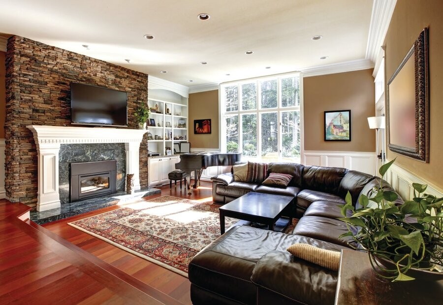 A living room space featuring seating, a TV mounted above a fireplace, and in-ceiling lighting fixtures.