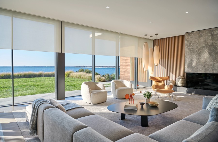 Lutron roller shades partially lowered on floor-to-ceiling windows overlooking a lakefront backyard